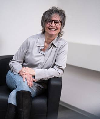 Teammitglied in heller Kleidung, entspannt sitzend mit freundlichem Lächeln im Büroumfeld